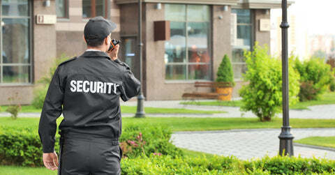 Male security guard talking on walkie talkie outside of a commercial building